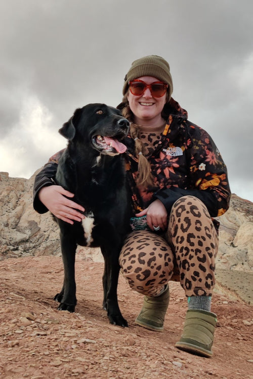 Ali is posing with her lab/collie mix dog, Meru. Meru has her mouth open and her tongue hanging out.