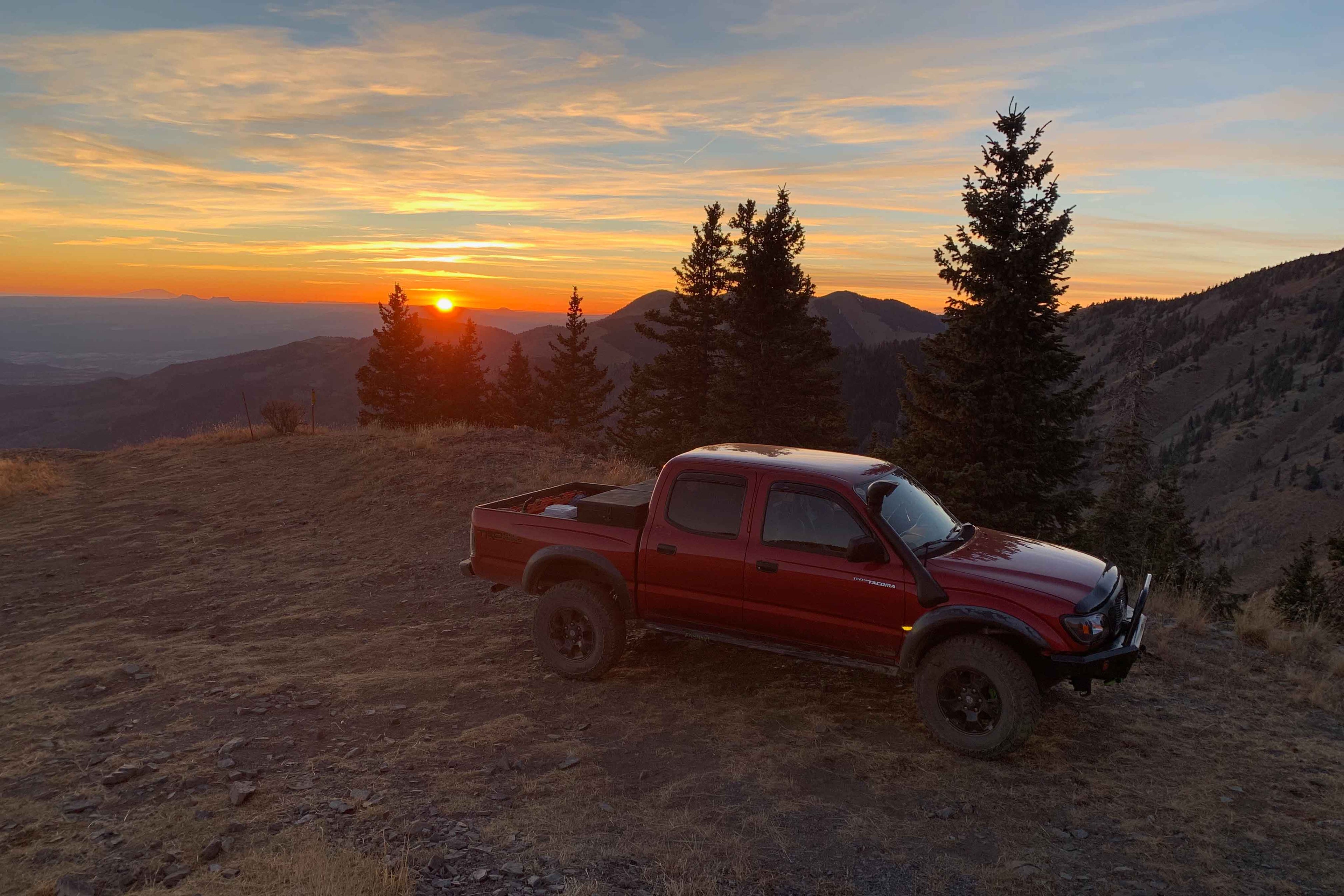 red Toyota Tacoma parked on a cliffside at sunset in San Juan County, UT